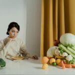 Kobieta przy stole z warzywami, uważnie planująca zdrową porcję