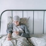 Kobieta w trakcie chemioterapii leży w szpitalnym łóżku i korzysta z telefonu