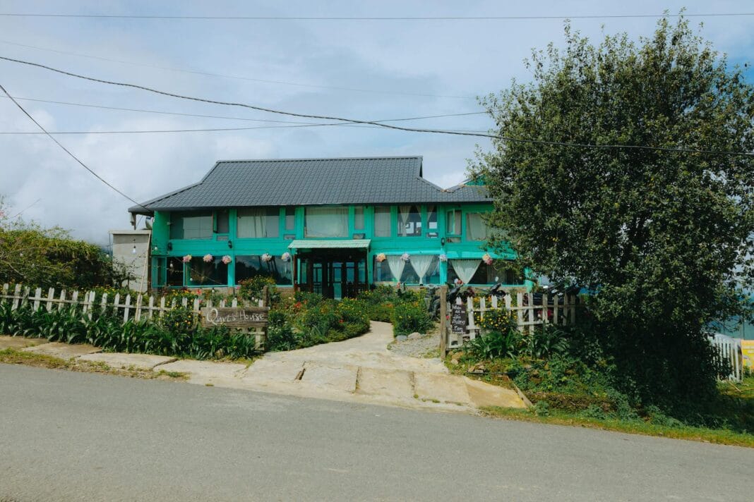 Zielony pensjonat agroturystyczny wśród drzew przy spokojnej wiejskiej drodze Zielony pensjonat agroturystyczny wśród drzew przy spokojnej wiejskiej drodze