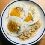 Spaghetti z sadzonymi jajkami na talerzu, posypane świeżo mielonym pieprzem