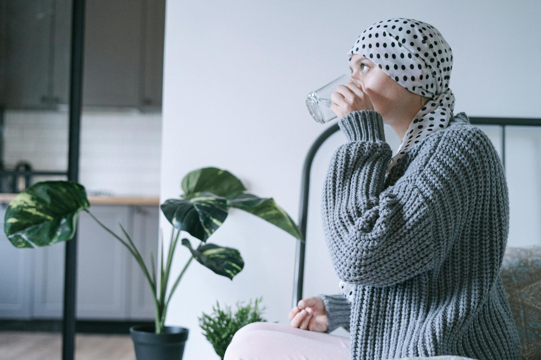 Kobieta w chuście na głowie pije szklankę wody w domu