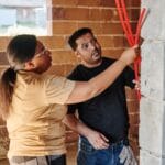 Dwaj elektrycy sprawdzają instalację elektryczną w murze